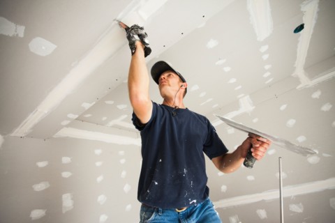 Drywall worker taping and mudding joint in ceiling. Photo: Mike Kemp