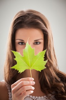 Beautiful woman holding green sycamore leaf in front of mouth and nose. Photo: Mike Kemp