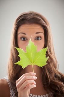 Beautiful woman holding green sycamore leaf in front of mouth and nose. Photo: Mike Kemp