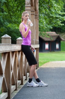 Young woman leaning against a bridge after running and drinking water from a bottle