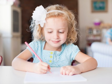 Girl drawing at table and smiling. Photo: Jessica Peterson