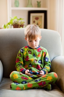 Boy in his pijamas sitting on armchair and playing video game.. Photo : Jessica Peterson