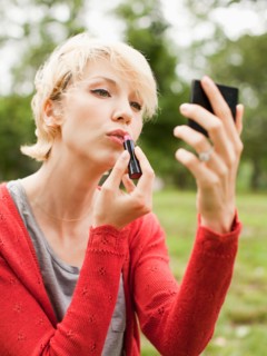 Woman holding mirror and using lipstick. Photo: Jessica Peterson