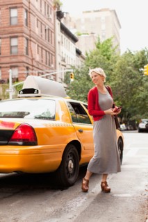 Woman standing next to yellow taxi on street. Photo : Jessica Peterson