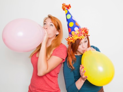 Studio Shot, Two young women blowing up pink and yellow balloons. Photo : Jessica Peterson