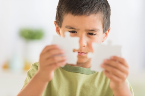 Boy (6-7) holding jigsaw pieces.