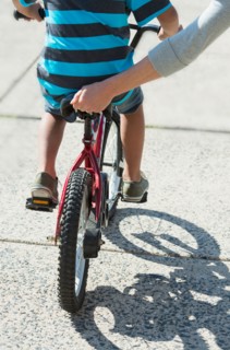 Mother helping boy (6-7) ride bicycle.