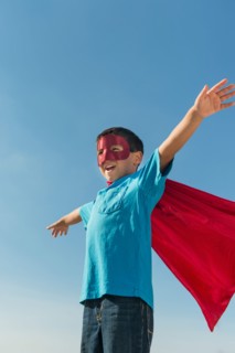 Boy (6-7) in superhero costume under blue sky.