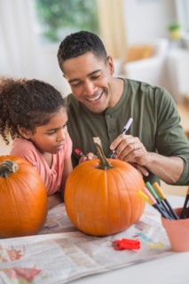 Father and daughter (6-7) carving pumpkins for Halloween.