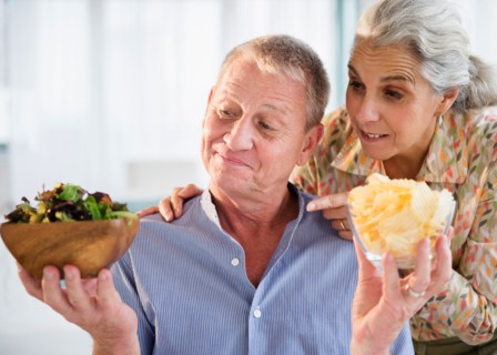 Elderly couple choosing between fresh salad and crisps