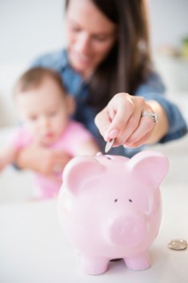 Mother with daughter (6-11 months) putting coins into piggybank
