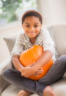 Portrait of smiling girl (6-7) sitting on sofa with pumpkin