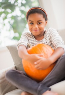 Portrait of smiling girl (6-7) sitting on sofa with pumpkin