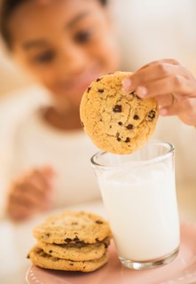 Girl (6-7) having cookie and milk