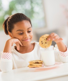 Girl (6-7) having cookie and milk