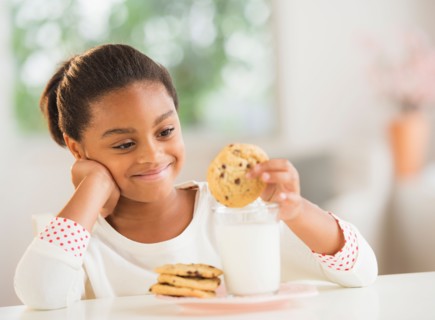 Girl (6-7) having cookie and milk