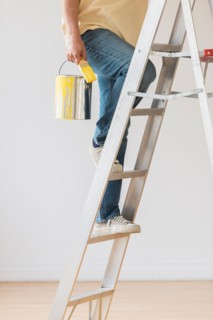Man holding paint can and climbing ladder.