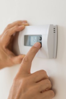 Hand changing settings on air conditioning thermostat.