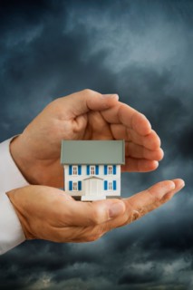 Hands holding model house in front of stormy sky.