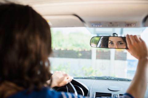 Woman adjusting rear view mirror in car. Photo: Jamie Grill