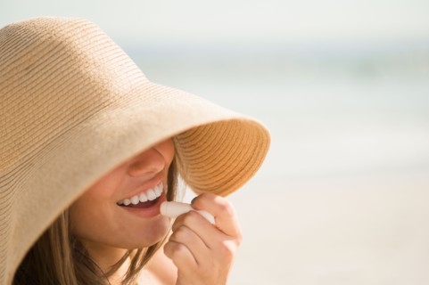 Woman wearing sun hat applying lipstick. Photo : Jamie Grill