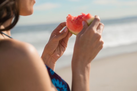 Woman eating watermelon at beach. Photo : Jamie Grill