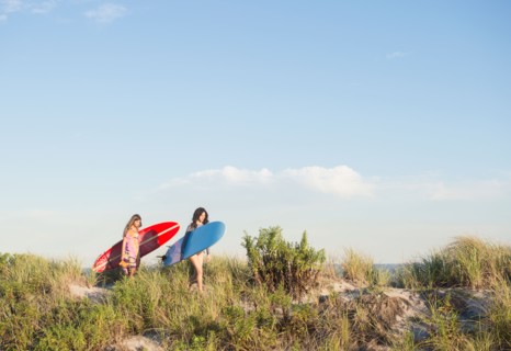 Two female surfers walking on beach. Photo : Jamie Grill