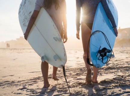 Two female surfers walking on beach. Photo : Jamie Grill