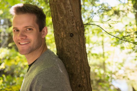 Portrait of young man leaning against tree trunk. Photo: Jamie Grill