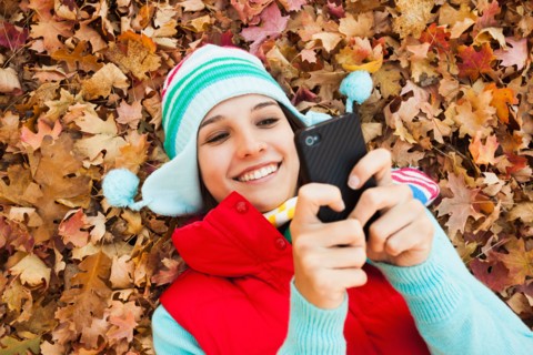 Young woman lying on autumn leaves and using . Photo : Mike Kemp