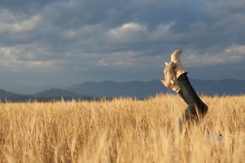Woman lying in scenic field with feet in air. Photo : Noah Clayton