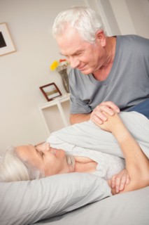 Bedroom scene with senior man holding wife's hand. Photo: Rob Lewine