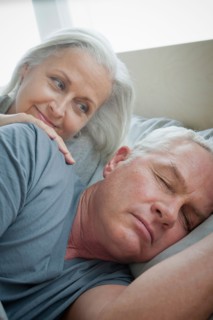 Senior woman looking at sleeping husband. Photo : Rob Lewine