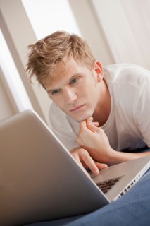 Man lying on bed using laptop. Photo: Rob Lewine