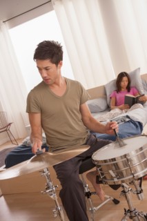 Man plying drums and woman reading in bed. Photo : Rob Lewine