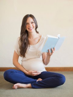 Pregnant mid adult woman sitting with crossed legs and holding book. Photo : Jessica Peterson