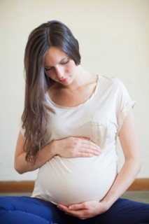 Pregnant mid adult woman looking down and touching her abdomen. Photo: Jessica Peterson