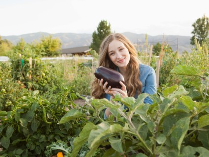 Portrait of young woman harvesting eggplant. Photo: Jessica Peterson