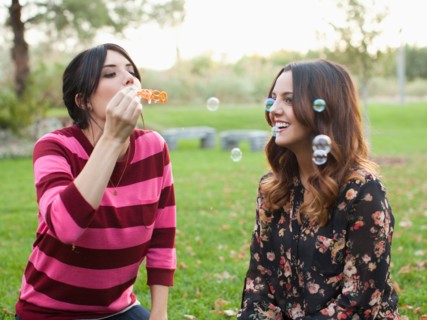 Two young women blowing bubbles in park. Photo : Jessica Peterson