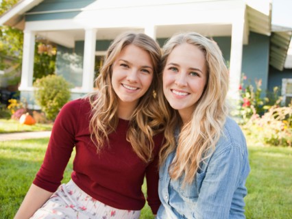Portrait of two young women cheek to cheek in front of house. Photo : Jessica Peterson