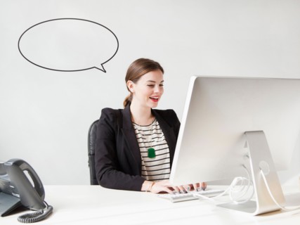 Studio shot of young woman working on computer with speech bubble next to her head. Photo: Jessica