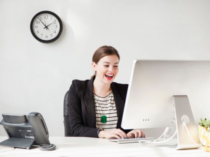 Studio shot of young woman working on computer and laughing. Photo : Jessica Peterson