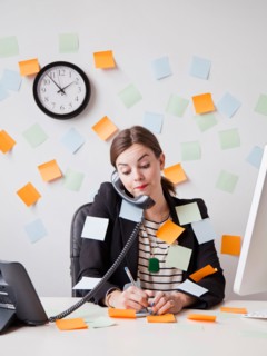 Studio shot of young woman working in office covered with adhesive notes. Photo: Jessica Peterson