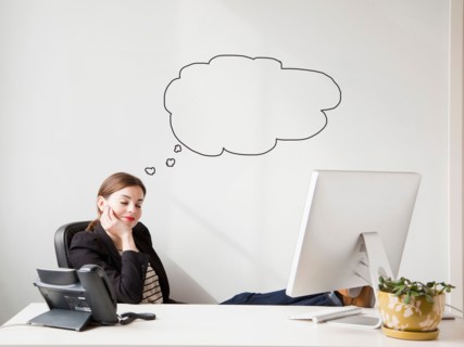Studio shot of young woman working at desk with thought bubbles next to her head. Photo : Jessica