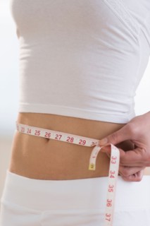 Midsection of woman measuring waistline.