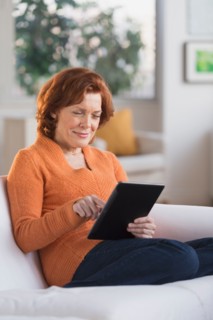 Woman sitting on sofa using digital tablet.