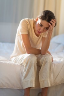 Young woman sitting on bed with headache.