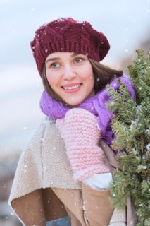 Portrait of young woman wearing knit hat, gloves and scarf an carrying fir wreath.