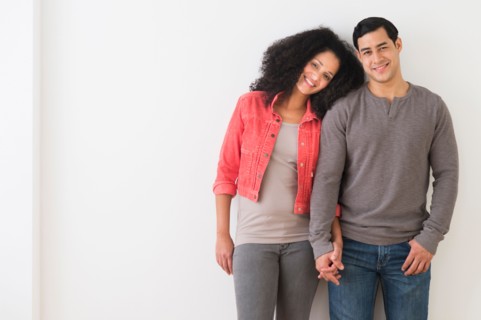 Portrait of smiling couple standing against white wall.