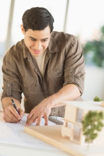 Male architect working with blueprint and model home.